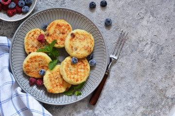 Cheesecakes with berries and honey for breakfast on a gray concrete background. View from above.