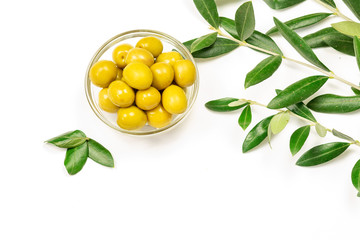Some fresh canned olives in a glass bowl with olive leaves on the white background.