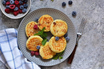 Cheesecakes with berries and honey for breakfast on a gray concrete background. View from above.