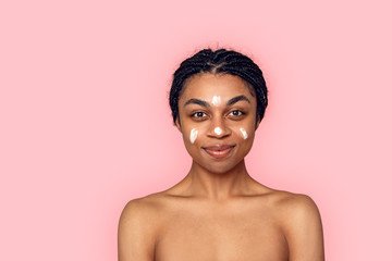 Beauty Concept. Young african woman isolated on pink having cream on face looking camera smiling happy