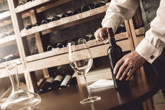 Sommelier Concept. Senior man standing opening wine bottle close-up