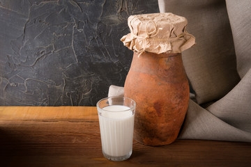 A glass of fresh milk and a clay jug on a wooden table.