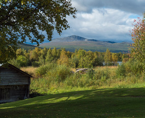 Traditional wooden cabin with view on beautiful landscape of Sarek mountains and river Kamajokk in Kvikkjokk in Swedish Lapland. Summer sunny day, golden hour, dramatic clouds