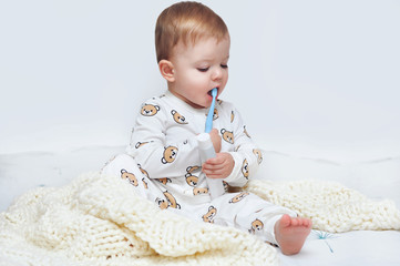 Little baby boy sitting in his pajamas in bed with a toothbrush in his hand and smiling showing his...