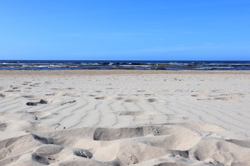 Fototapeta na wymiar Wavy sand with footsteps on baltic sea coast with wave and blue sky 