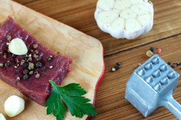 head of garlic hammer for a chop and a piece of meat on wooden background, concept of cooking steak