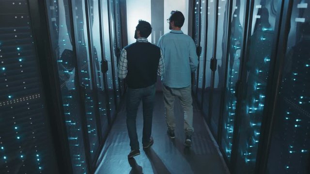 Two server technicians walking in server rack corridor at data center discussing work or future plans. Teamwork. Computer security office.