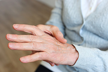 Elderly woman applying moisturizing lotion cream on hand palm, easing aches. Senior old lady experiencing severe arthritis rheumatics pains, massaging, warming up arm. Close up, copy space, background