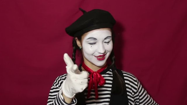 Beautiful mime girl nods her head affirmatively and says yes while looking at the camera. Beautiful mime girl in a striped shirt nods her head affirmatively and smiles. Portrait on a red background.