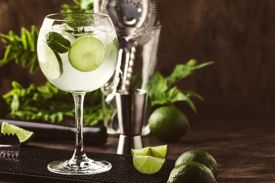 Martini royale alcoholic cocktail with white vermouth, prosecco, lime, mint and ice. Old wooden table background, bar tools, selective focus. All names refer to cocktails, not trademarks