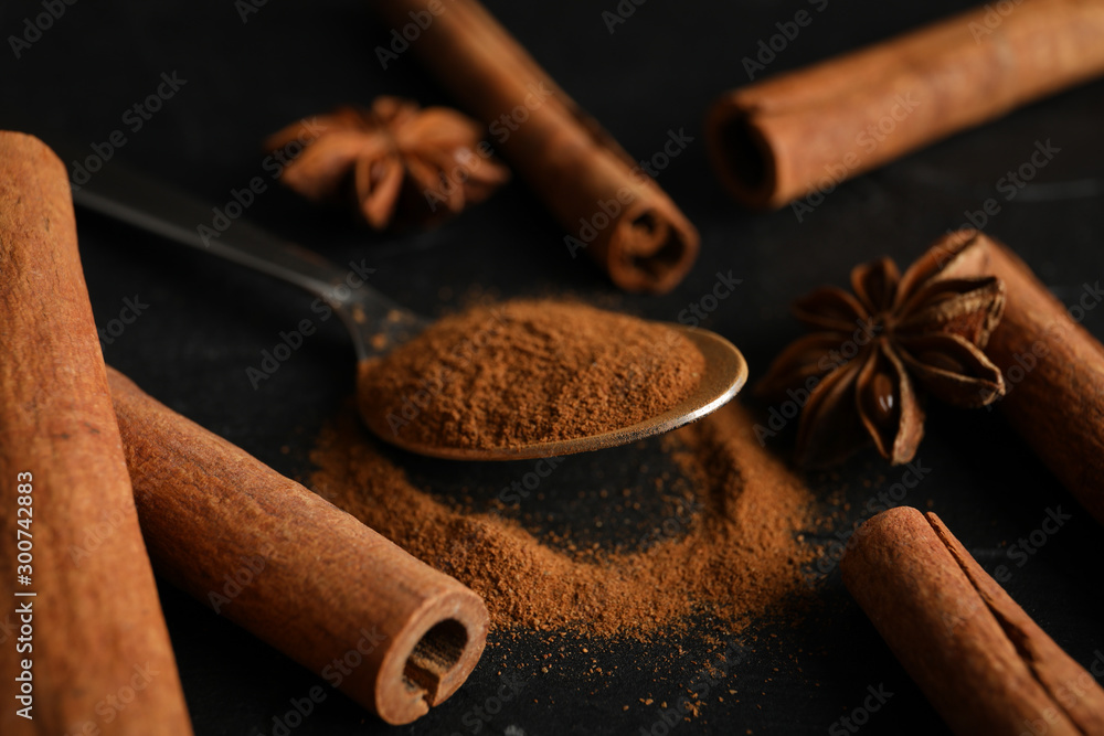 Poster Cinnamon sticks, anise and spoon on black background, space for text