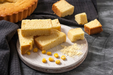 Freshly baked corn bread on a round wooden white board with corn on a dark background with a black napkin. Traditional pastries in US national cuisine.