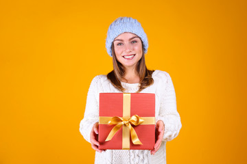 Close up portrait of a young beautiful woman with light make up on, wearing knitted sweater & blue woolen beanie. Attractive female in winter knitwear outfit, isolated on yellow background. Copy space