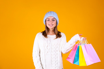 Close up portrait of a young beautiful woman with light make up on, wearing knitted sweater & blue woolen beanie. Attractive female in winter knitwear outfit, isolated on yellow background. Copy space