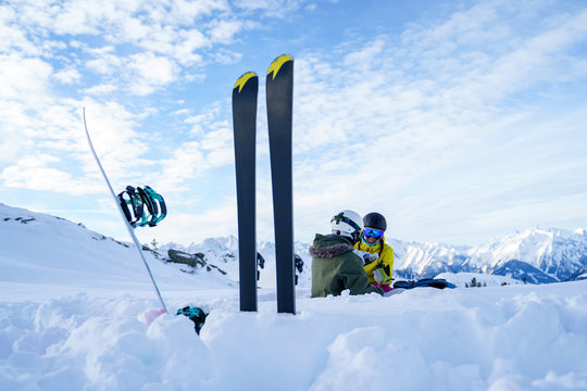 Image of skis, ski poles against background of two sports women with thermos sitting in ski resort in winter.
