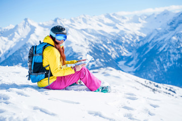 Fototapeta na wymiar Photo of snowboarder woman in helmet with map in her hands sitting on mountain slope.