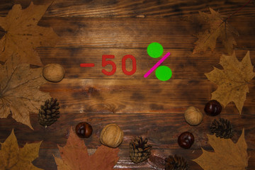 Autumn Sale 50 Percent Discount. The inscription on a dark wooden background in a frame of colorful autumn leaves. Top view.