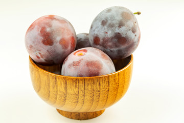 Some of ripe whole plums in the wooden bowl in the white background.
