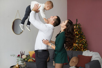 Stylish happy couple and the cute little baby boy have fun at Christmas interior. Young parents with little son celebrating New year. Holidays of beautiful young woman, handsome man and their son.