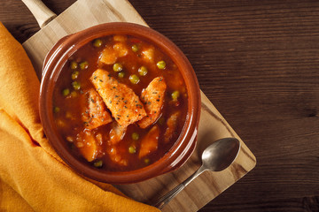 Top view of a clay pot with a delicious fish stew with peas and cooked potatoes with a vintage...