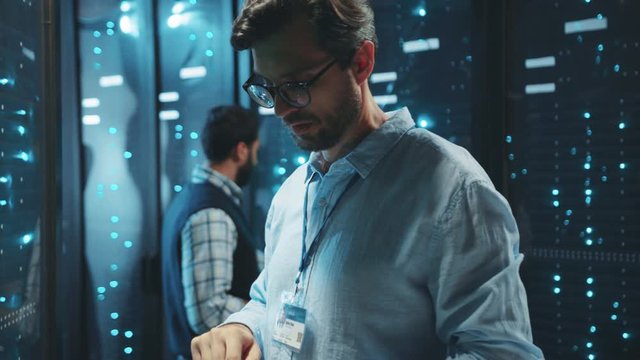 IT technician in data center digital server room controlling work of rack server cabinets with a tablet. Professional server engineer at work.