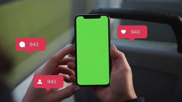Close up of a woman's hand holding a mobile telephone with a vertical green screen in tram chroma key smartphone technology. Animation with User Interface - Likes, Followers, Comments for Social Media