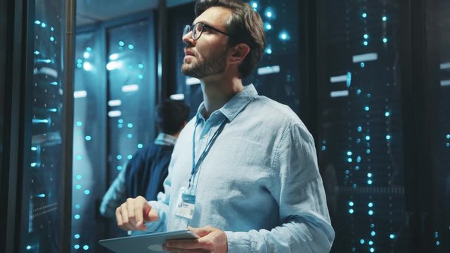 Server administrator in glasses using digital tablet updating hardware of server rack cabinets at data center. Computer service. Cyber security.