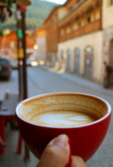 Closeup Texture of Half Cup of Hot Cappuccino Coffee in Woman's Hand against Blurry Old Town