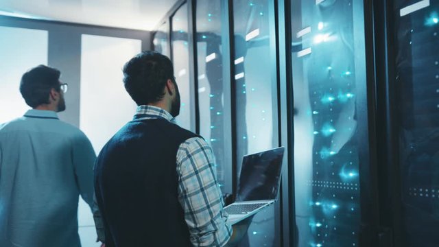In data center two caucasian server engineers inspecting network data cabinets working on rack. Computer security. Teamwork and collaboration.