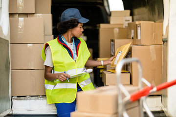 Female African American deliverer sorting packages in a van.