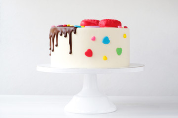 White cake decorated with colorful hearts, confectionery sprinkles and drenched in chocolate on a white background.