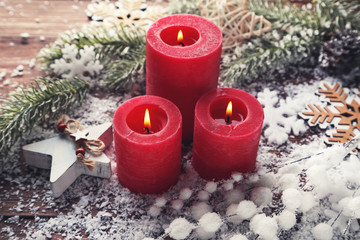 Christmas candles with snow and fir tree branches on brown wooden table