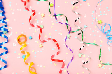 Colorful ribbons confetti and paper stars on pink background