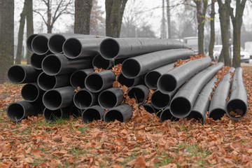 Prepared black polyethylene pipes for sewage are lying on the ground with yellow leaves