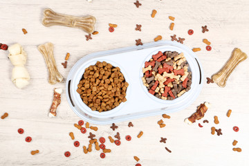 Dry pet food in bowls with bones on the floor
