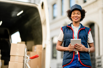 Portrait of happy African American delivery woman with a touchpad outdoors.