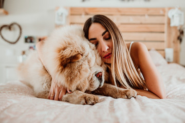 .Pretty young woman playing with her chow chow dog. Lying in bed relaxed and carefree. Sharing happiness and love. Lifestyle