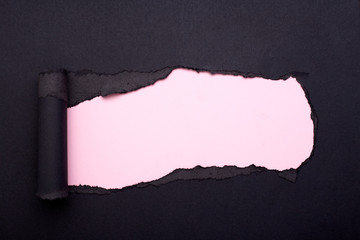 Hole in the black paper. Torn. Pink paper background. Abstract background.