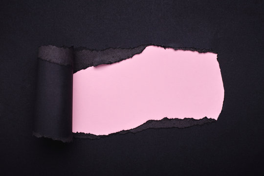 Hole in the black paper. Torn. Pink paper background. Abstract background.