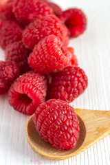 Close-up of red raspberries on white wooden board, with wooden spoon in the foreground and blur in the background. In vertical