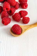 Top view of red raspberries on white wooden board, with wooden spoon in the foreground. In vertical