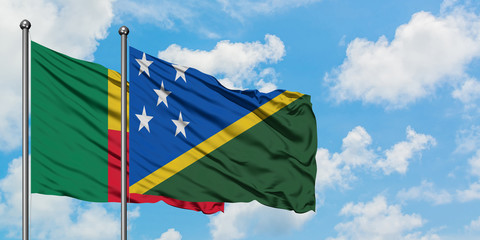 Benin and Solomon Islands flag waving in the wind against white cloudy blue sky together. Diplomacy concept, international relations.