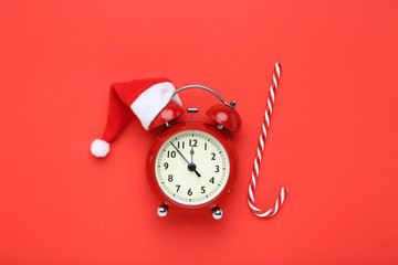 Alarm clock with santa hat and candy on red background