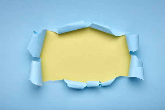 Hole in the blue paper. Torn. Yellow background. Abstract background.