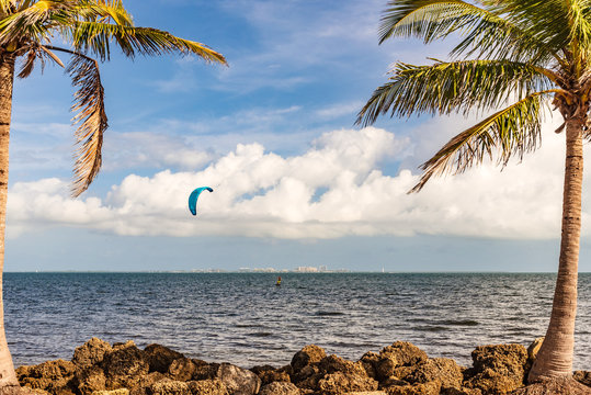 A kitesurfer on Biscayne Bay sailing across the water with Key Biscaye's skyline on the horizon. Miami, Florida