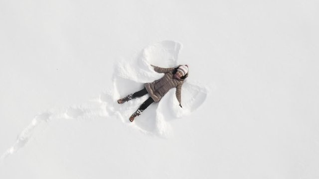 Asian woman playing in the snow and making snow angels.