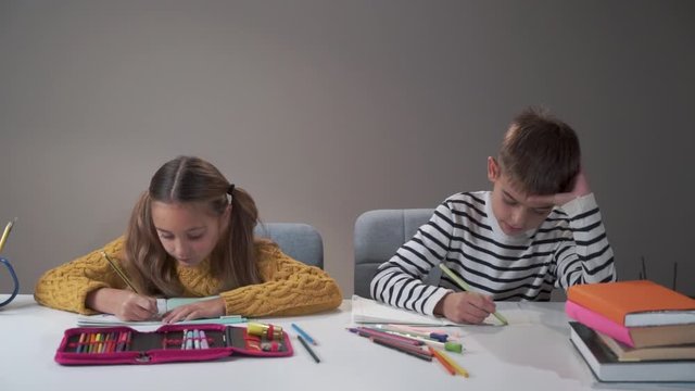 Two classmates studying at school. Tired bored boy banging head against the table. Difficulties in education process, bad behaviour.