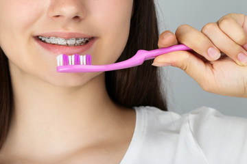 Young girl with dental braces holding toothbrush on grey background