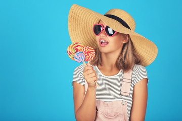 Young girl wearing sunglasses, hat and holding lollipops on blue background