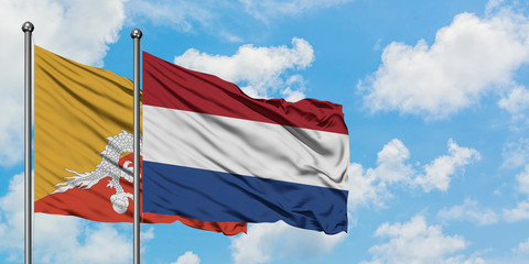 Bhutan and Netherlands flag waving in the wind against white cloudy blue sky together. Diplomacy...